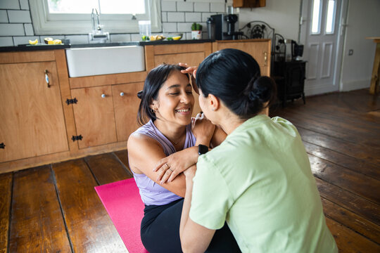 Two women relaxing after home workout on yoga mat in kitchen