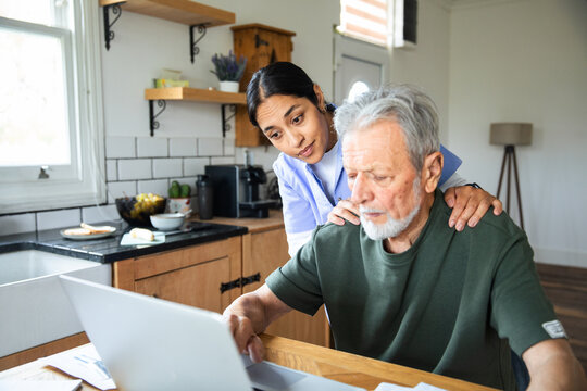 Caregiver assisting senior man on laptop in home kitchen