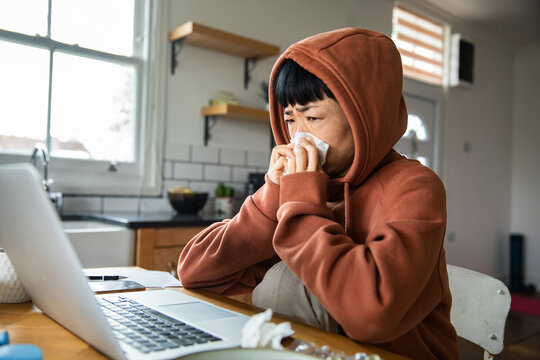 Sick person blowing nose while working at home kitchen table