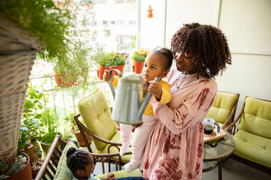 Mother helping toddler water balcony plants at home