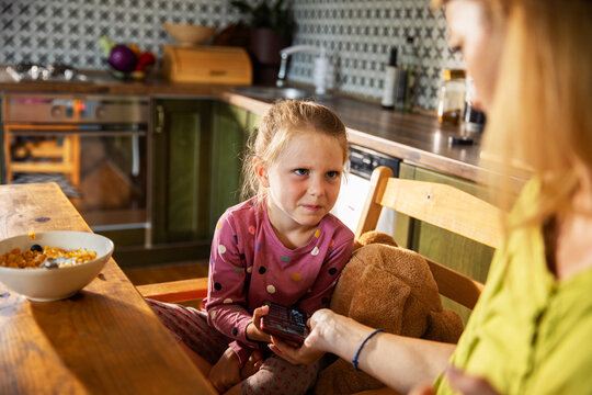 Parent limiting daughter's screen time at breakfast in home kitchen