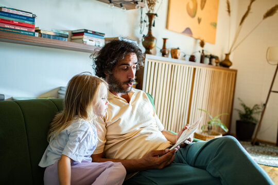 Father and daughter reading a book on the living room sofa