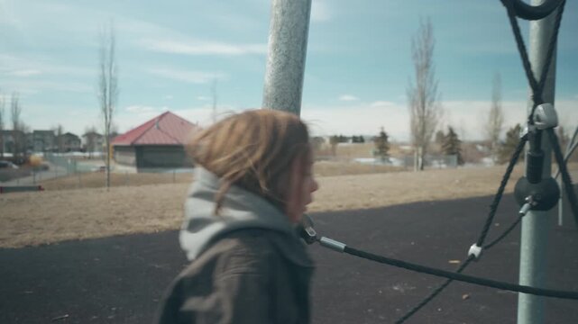 Boy climbing metal bars and grabbing ropes on playground structure from behind