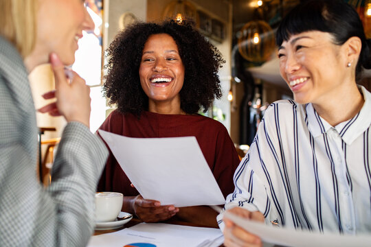 Smiling businesswomen discussing documents at cafe