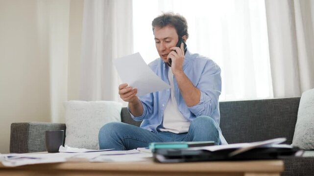 Stressed man arguing on phone over unpaid utility bills and rising energy prices. Overwhelmed by household expenses, he reacts to overdue bills in shock. High quality 4k footage