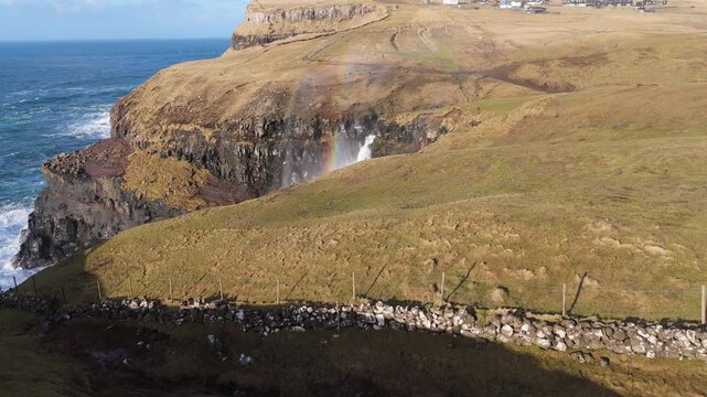 フェロー諸島の断崖から海へ落ちる滝と虹、風に舞う飛沫の空撮（Faroe Islands Coastal Waterfall and Rainbow Aerial）