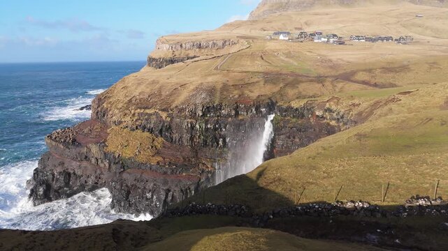 フェロー諸島ヴァーガル島、断崖から海へ落ちるムーラフォッスルの滝と村の空撮（Faroe Islands Mulafossur Waterfall Aerial 4K）