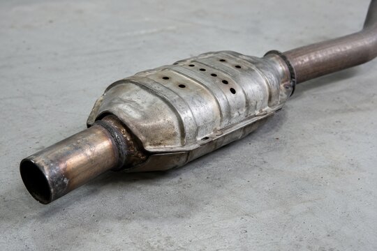 Used automotive catalytic converter and exhaust pipe resting on a concrete workshop floor