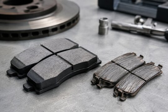 New and worn automotive brake pads compared on a mechanic's workbench during maintenance