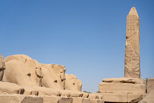 ncient Egyptian Avenue of Ram-headed Sphinxes with the obelisk of Pharaoh Thutmose I at Karnak Temple complex in Luxor Egypt, featuring sandstone sculptures, hieroglyphic inscriptions and historic tem