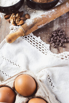 Top view of fresh organic eggs with baking ingredients, including flour, chocolate chips, almonds, and walnuts, scattered on a rustic wooden background, ready for a healthy recipe.