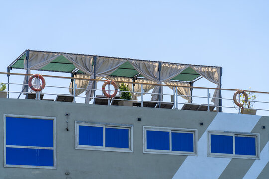 Rooftop deck with cabanas, lounge chairs, and life preservers on clear day, featuring striking blue windows on building below
