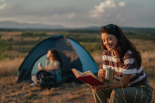 Woman reading book and drinking coffee camping outdoors