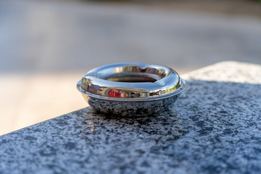 Polished Chrome Circular Ashtray Resting on Speckled Granite Surface Outdoors During Golden Hour, Capturing Subtle Reflections of Surrounding Environment