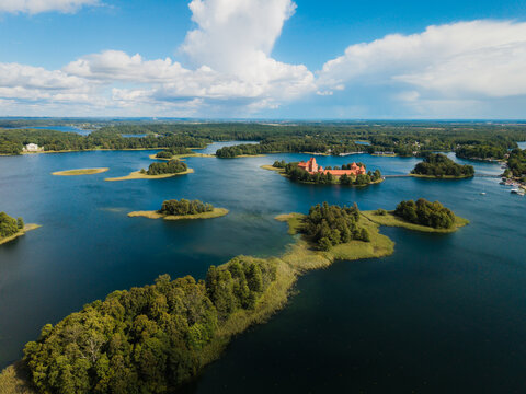 Aerial view of Trakai Island Castle surrounded by the blue waters of Lake Galve, lush green islands, and a bright sky in Trakai, Vilnius County, Lithuania.