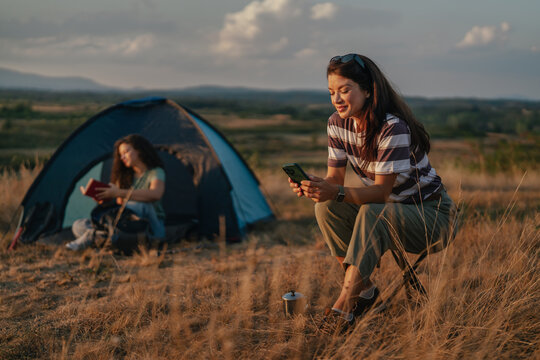 Young woman using smartphone while camping at sunset