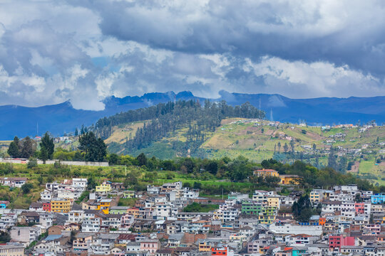 Colorful colorful houses and dense residential buildings built on the hillside slopes in Quito, Ecuador, against Andean mountain background.