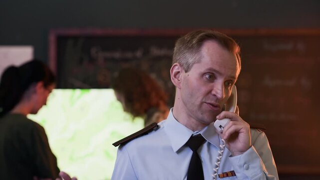 Middle-aged Caucasian military officer talking on corded telephone in command center while colleagues work in background. Clip is ideal for defense industry videos or corporate security training