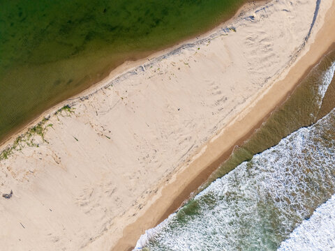 Aerial view of a pristine sandbar separating the calm green waters of a lagoon from the crashing white waves of the ocean in Pacitan, East Java, Indonesia.