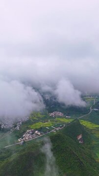 Vertical Video: Autumn rice harvest with golden paddies and village scattered below a layer of morning clouds