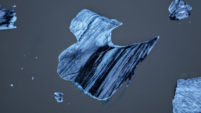 Aerial view of icebergs with dark volcanic ash streaks floating in the glacial lagoon of Fjallsarlon in Hofn, Sveitarfelagid Hornafjordur, Iceland.