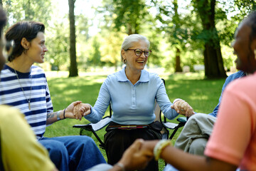 Fototapeta premium Senior Caucasian female therapist holding hands with diverse group of people during outdoor support session in park, representing mental health and community therapy services