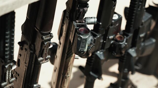 Several rifles of different types arranged vertically in a gun rack at an outdoor shooting range.