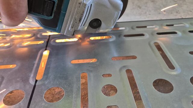 Slow motion side close-up of a worker cutting a cable tray longways with a hand angle grinder, creating a dramatic shower of sparks.