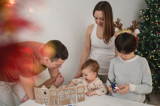 family with children cutting out paper Christmas tree ornaments in living room. A cozy weekend, time spent with the kids. Blurry, out-of-focus photos, background, lifestyle, live photos, real people