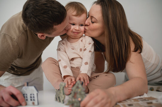 Mom and Dad kissing their little one at the same time at home. Playing with babies, spending time with family, celebrating holidays together. Winter games, crafts