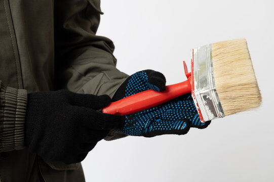 Close-up of a worker wearing gloves and holding a wide paint brush, illustrating home renovation, decorating and construction work.