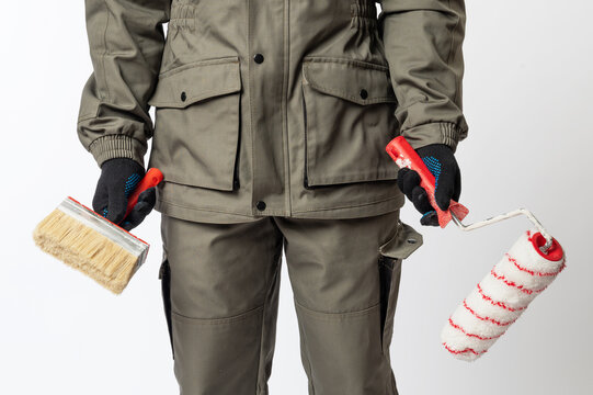 Construction worker in protective clothing holding paint brush and roller, ready for home renovation, decorating or professional painting work.