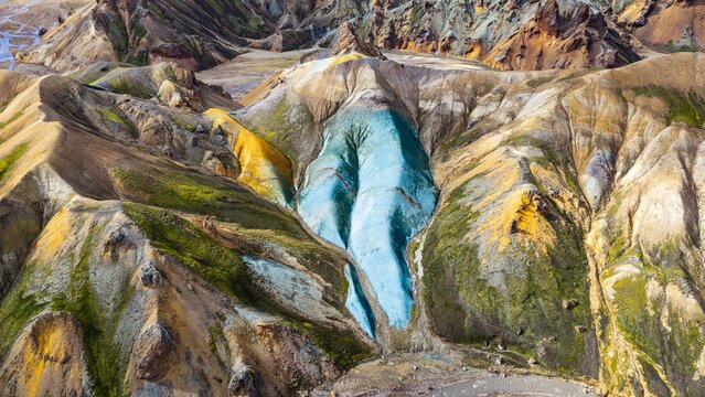 Aerial view of the vibrant Graenihryggur ridge featuring striking blue-green rhyolite rock formations surrounded by moss-covered slopes and rugged volcanic terrain in Rangarthing ytra, Iceland.