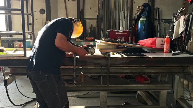 Professional craftsman grinding a metal part on a workbench. Backlit scene with flying sparks in a busy industrial manufacturing facility