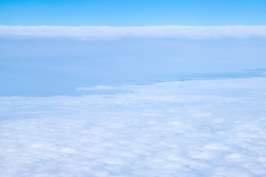 An aerial view from an airplane window looking out over a thick, rolling layer of low-level clouds beneath a clear blue sky. A vast sheet of white, textured clouds, typical of a low cloud layer. 