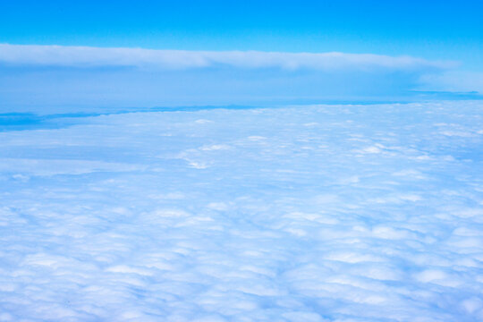 An aerial view from an airplane window looking out over a thick, rolling layer of low-level clouds beneath a clear blue sky. A vast sheet of white, textured clouds, typical of a low cloud layer. 