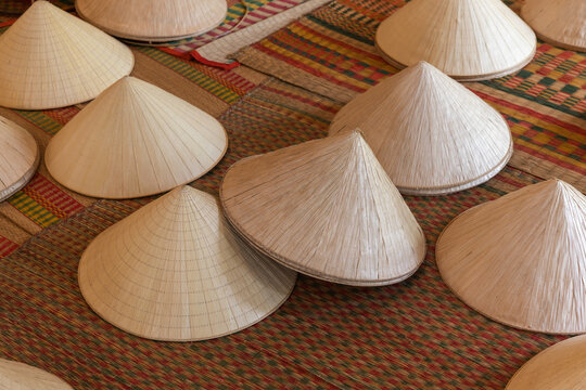 Rows of traditional Vietnamese conical hats Non La made of woven straw arranged on colorful woven mats, evoking craftsmanship, cultural heritage and market life in Southeast Asia