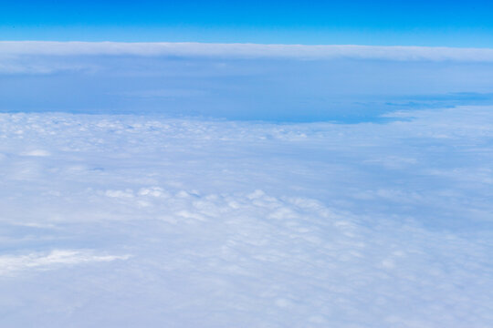 An aerial view from an airplane window looking out over a thick, rolling layer of low-level clouds beneath a clear blue sky. A vast sheet of white, textured clouds, typical of a low cloud layer. 