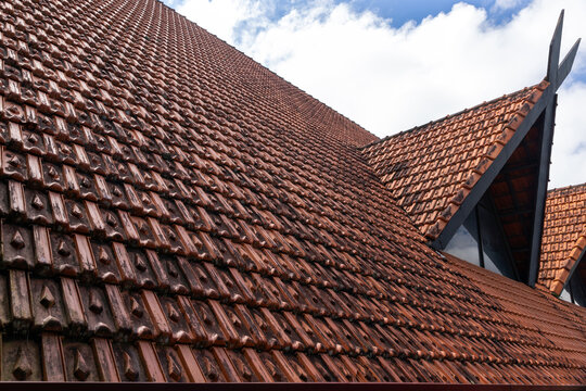 Angled view of terracotta roof tiles on a traditional building showing repeating geometric pattern, triangular gables and weathered texture. Warm earthy tones and strong diagonal lines