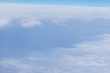 Fototapeta premium An aerial view of a blue sky and soft white clouds, captured from an airplane window. Light blue, clear upper atmosphere. Layered, soft white cloud cover spreading across the view. 