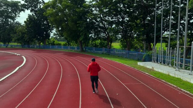 Drone view of a man running on an outdoor stadium track while challenging himself to reach fitness goals. The scene represents motivation, personal achievement, healthy lifestyle and active wellness.
