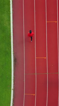Drone view of a man running on an outdoor stadium track while challenging himself to reach fitness goals. The scene represents motivation, personal achievement, healthy lifestyle and active wellness.
