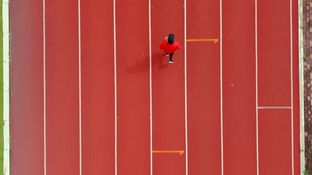 Drone view of a man running on an outdoor stadium track while challenging himself to reach fitness goals. The scene represents motivation, personal achievement, healthy lifestyle and active wellness.
