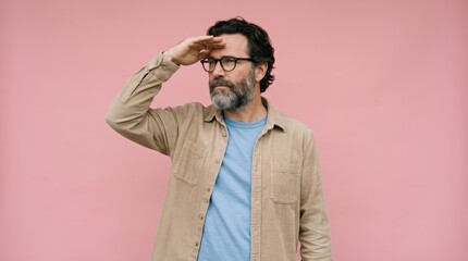 Fototapeta premium Portrait of a Stylish Mature Man Looking Far Away with Hand Over Eyes Against Pink Studio Background