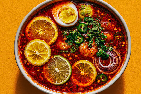 Spicy noodle soup bowl with citrus slices egg herbs and red chili oil