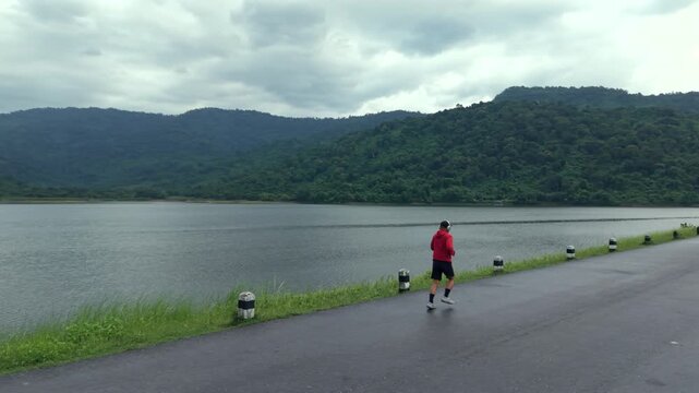 Drone view of a man running along a dam ridge during an outdoor workout. The scene represents fitness goals, personal challenge, determination, achievement and an active healthy lifestyle.
