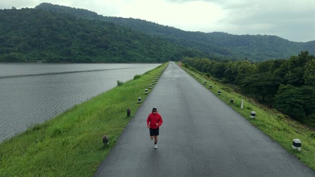 Drone view of a man running along a dam ridge during an outdoor workout. The scene represents fitness goals, personal challenge, determination, achievement and an active healthy lifestyle.
