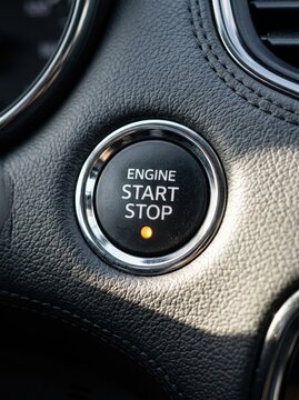 Close-up of a Modern Car Engine Start Stop Button with Orange Indicator Light on a Black Leather Dashboard
