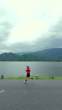 Drone view of a man running along a dam ridge during an outdoor workout. The scene represents fitness goals, personal challenge, determination, achievement and an active healthy lifestyle.
