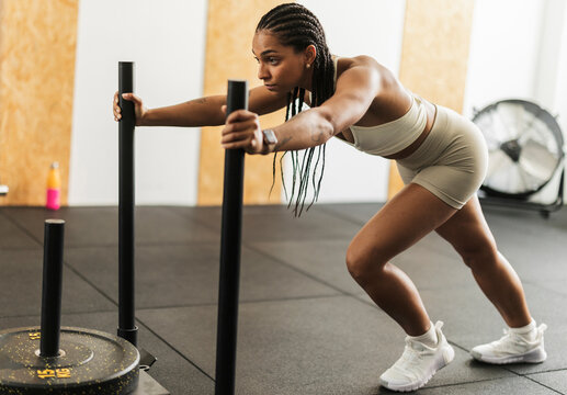 Woman pushing heavy weighted sled during intense gym workout